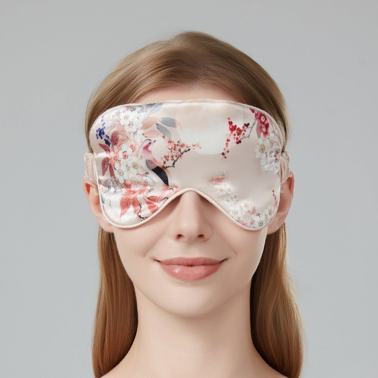 Woman wearing a floral sleep mask against a soft pink background