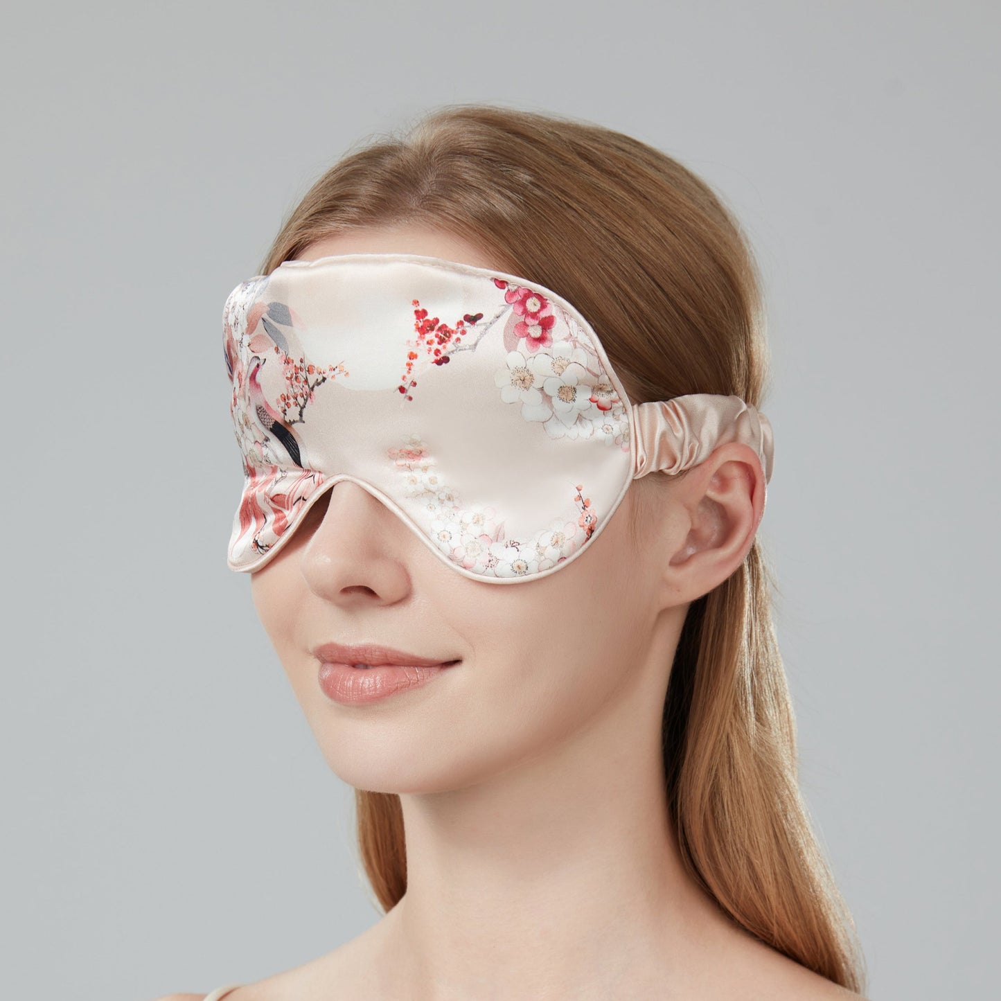 Woman wearing a floral sleep mask against a soft pink background
