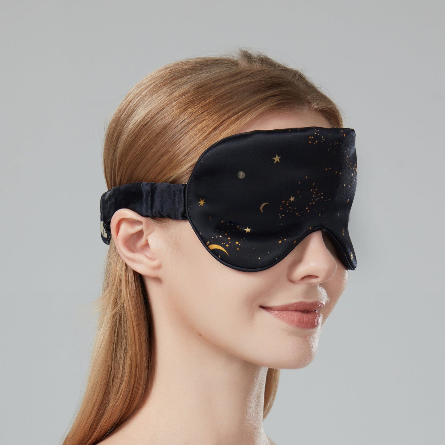 Woman wearing a black sleep mask with star and moon design on a dark navy background