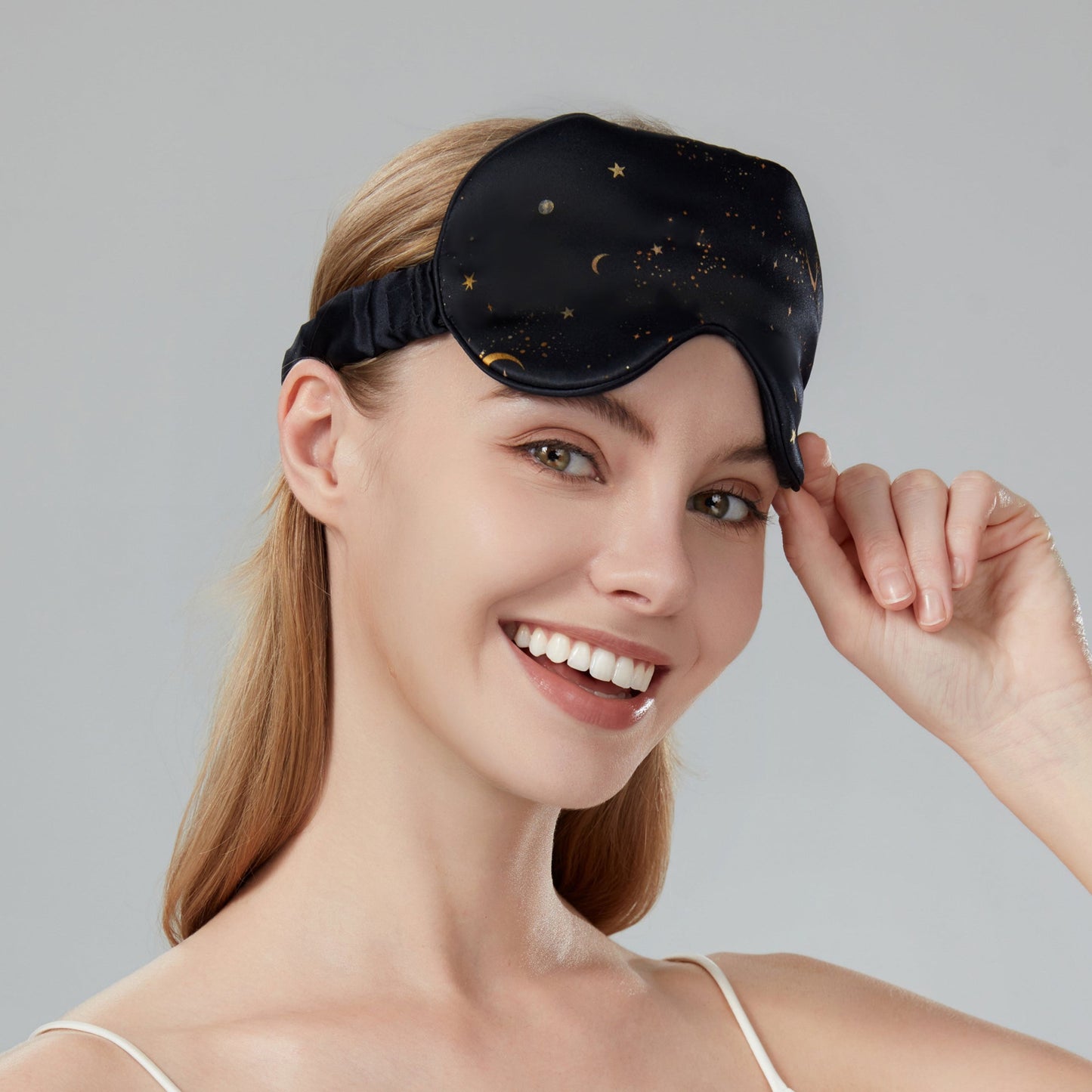 Woman wearing a black sleep mask with star and moon design on a dark navy background