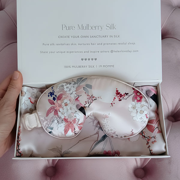 Silk eye mask with floral design in a box, held by a hand.