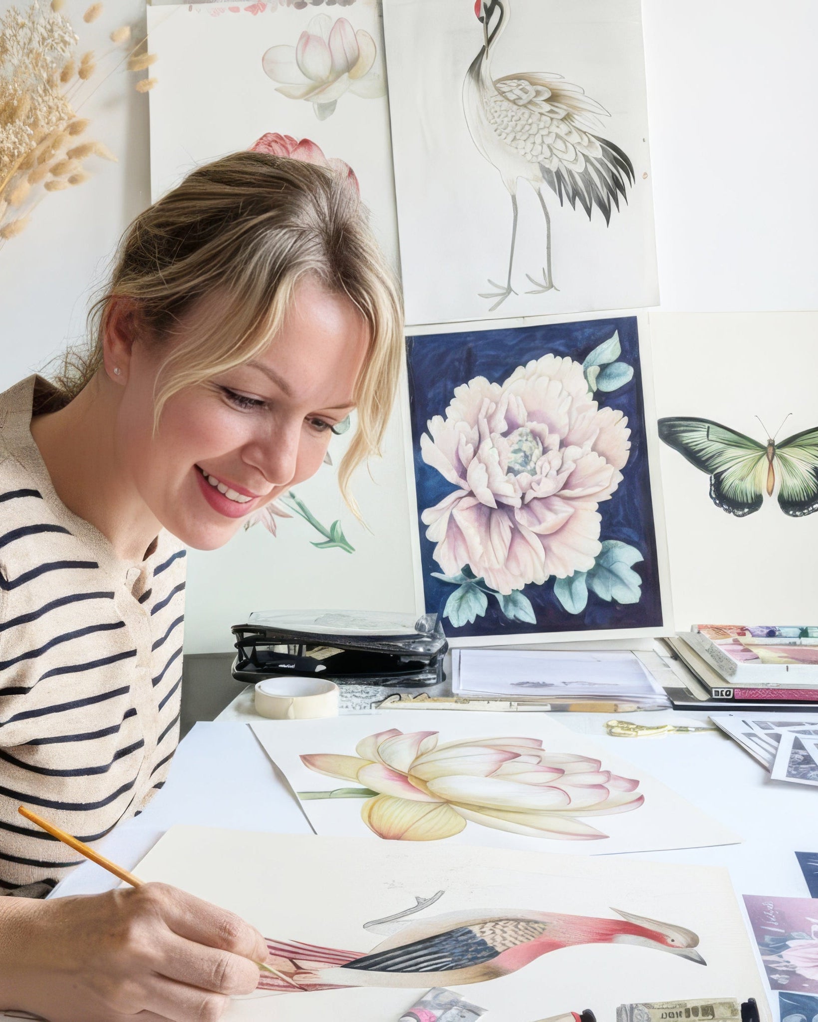 helen loveday sitting at a desk surrounded by art supplies and artwork, smiling.