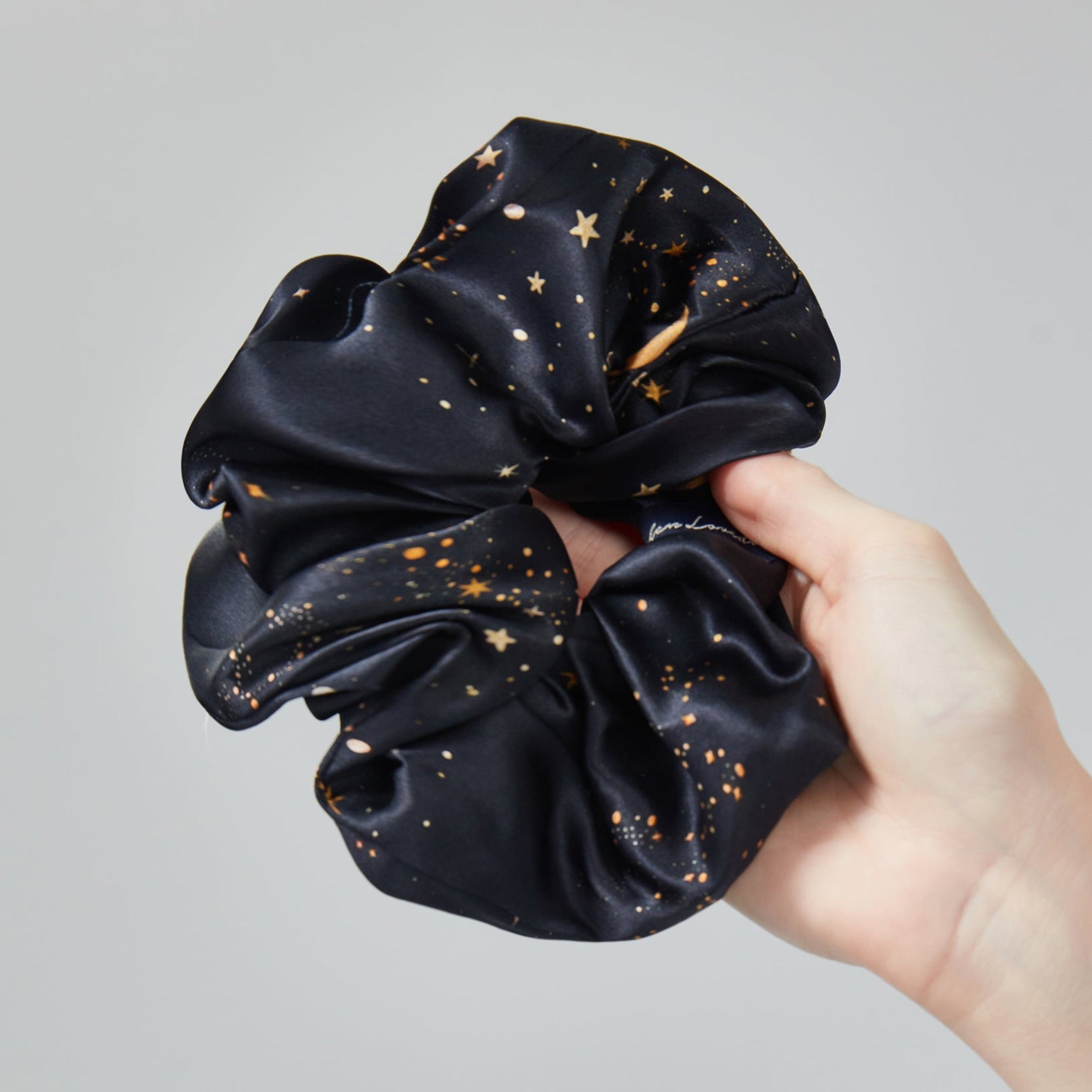 Black scrunchie with gold star pattern held by a hand