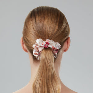 Woman with long blonde hair in a ponytail with a floral scrunchie against a gray background