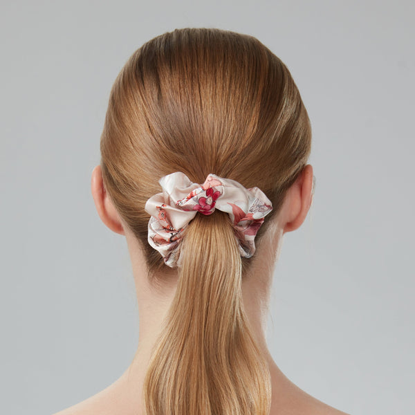 Woman with long blonde hair in a ponytail with a floral scrunchie against a gray background