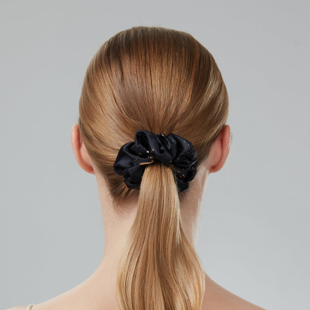Hand holding a black scrunchie against a gray background