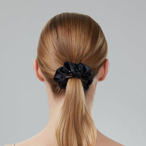 Woman with a ponytail wearing a black scrunchie on a gray background
