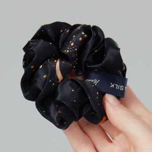 Hand holding a black scrunchie against a gray background
