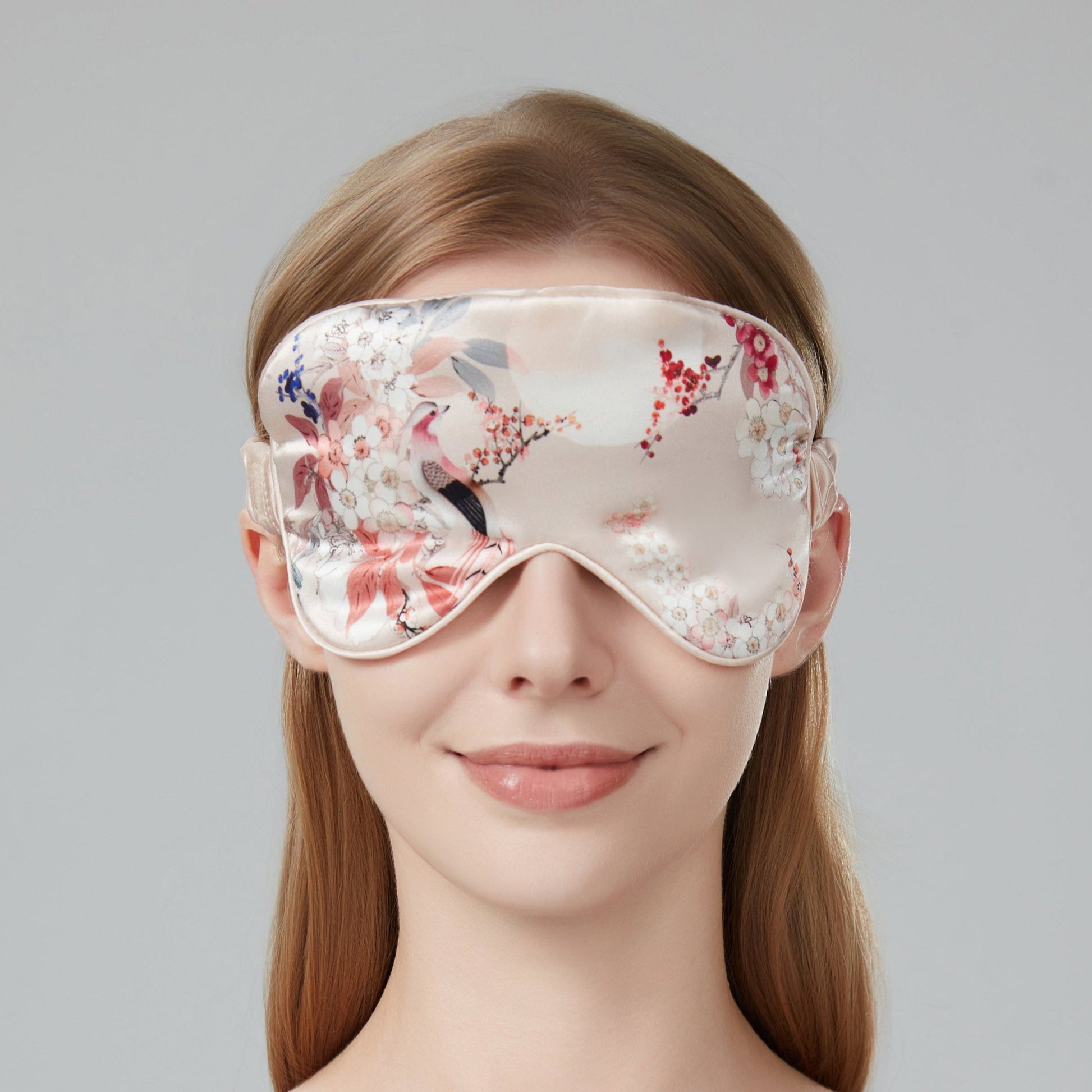 Woman wearing a floral sleep mask against a soft pink background