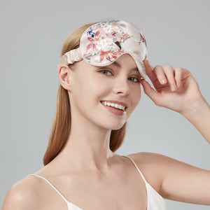 Woman wearing a floral silk sleep mask against a gray background