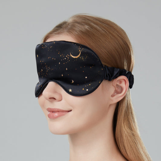 Woman wearing a black sleep mask with star and moon design on a dark navy background