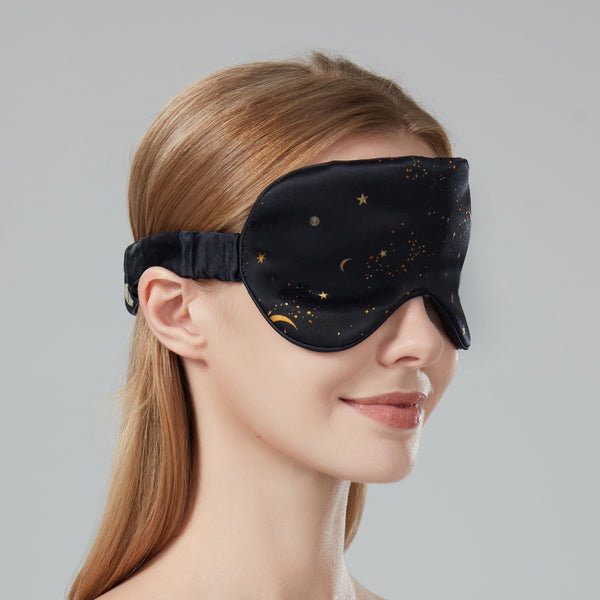 Woman wearing a black sleep mask with gold stars on a gray background